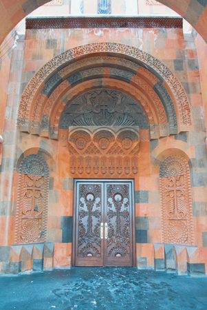 ABOVYAN, ARMENIA - DECEMBER 31, 2016: Decorated ornamental entrance door made with tuff stones to armenian cathedral Surb Hovhannes Church (St. John the Baptist Church) and a Khachkar (cross-stone).のeditorial素材