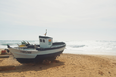 CABO DE GATA, SPAIN - FEBRUARY 9, 2016: An old vintage fishing boat with painted flags at the wild abandoned beach of national park Cabo de Gata, Almeria and brigh sea waves on the background.のeditorial素材