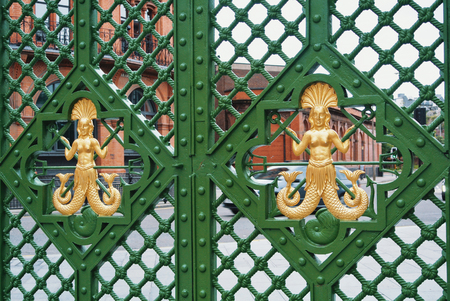 LIVERPOOL, ENGLAND - AUGUST 10, 2013: Close-up of a green metal ornamental gateway fence decorated with golden human sea figures with fish tails.のeditorial素材