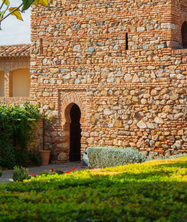 MALAGA, SPAIN - FEBRUARY 16, 2014: A courtyard with old medieval stone brick walls and arch entrance, plants and flowers at the gardens of the famous Palace Fortress of Alcazaba in Malaga, Andalusia.のeditorial素材