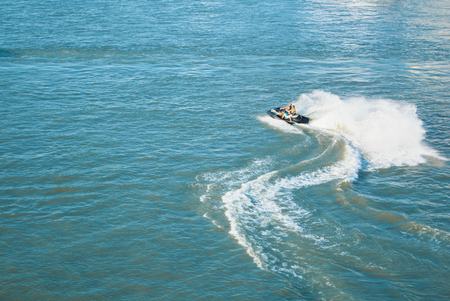 A top view of a couple turning riding having fun on jet ski wit a lot of splashes in blue transparent river sea water. Vacation concept with copy space for text.の写真素材