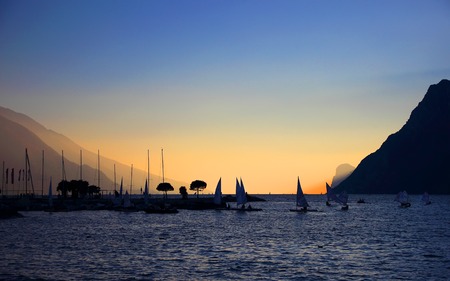 Sunset on a background of lake and sailing boats surrounded by mountains.の写真素材