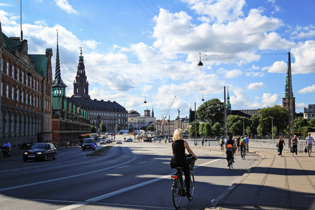 People riding bicycles on a street in Slotsholmen, view on a famous Old Stock Exchange -BÃ¸rsen. The tower with  "Dragon-spire" symbolizing the union of the Nordic countries - with three golden crownsのeditorial素材
