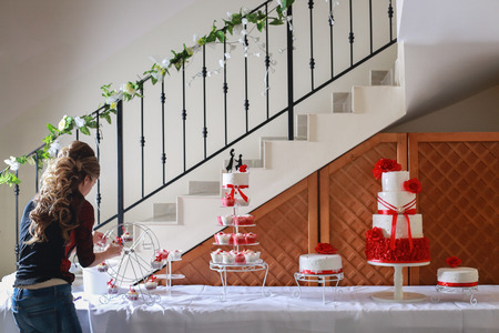 Confectioner stacking a 4 tier wedding cake at the reception place and decorating it with edible red marzipan flowersの写真素材