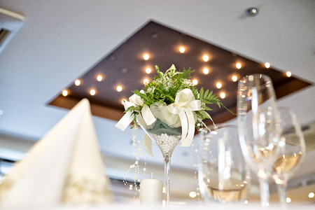 Wedding table decoration with white flower centerpiece, taken in hotel restaurant before wedding reception, spotlight on a ceiling at the background, napkin and empty whine and champagne glasses.の写真素材