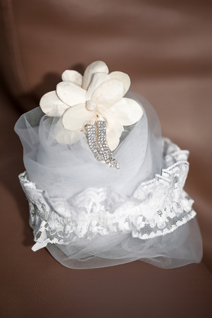 bridal accessories - laced garter, silver crystal hanging earrings and veil placed on brown leather sofaの写真素材