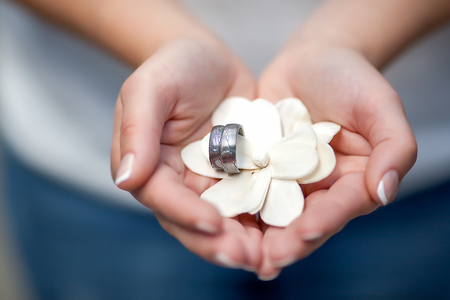 Female hands holding in a palms a wedding rings placed on white decorative flowerの写真素材
