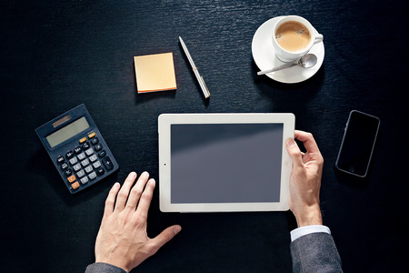 business man hands on a table with tablet, phone and cup of coffee in a officeの写真素材