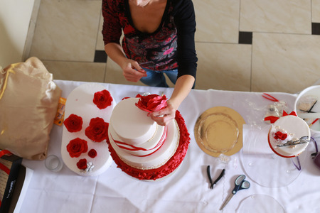 Confectioner stacking a 4 tier wedding cake at the reception place and decorating it with edible red marzipan flowersの写真素材