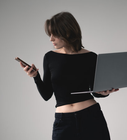 Elegant freelancer using phone while standing with laptop.