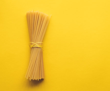 Bunch of spaghetti tied with string on yellow backgroundの写真素材