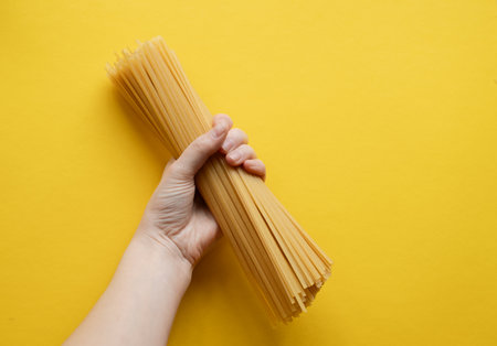 Hand holding dry noodles on yellow backgroundの写真素材