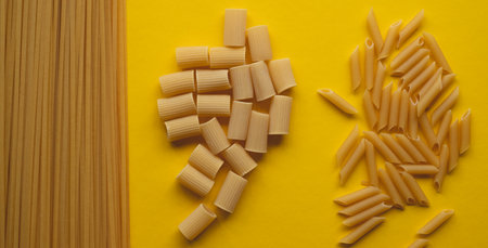 Variety of penne, cannelloni, and noodles on yellow surfaceの写真素材