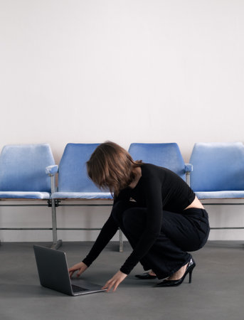 Woman squatting next to laptop on floor.の写真素材
