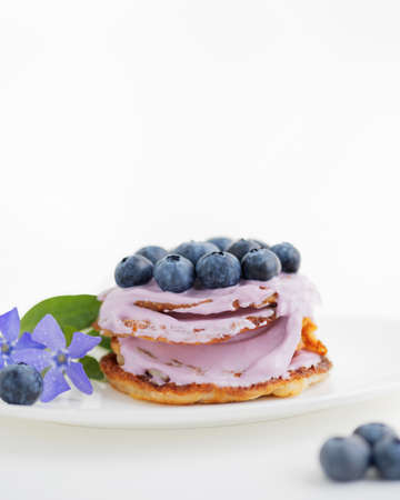 Pancakes with blueberries and yogurt on a white plate with violets flowers. White background with copy spaceの写真素材