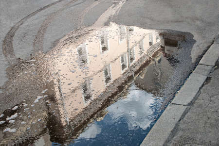 The reflection of the beige house in the surface puddles on the roadway tire tracks and bubbles