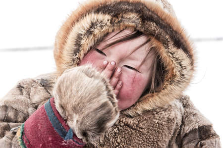 Yamal Peninsula, Russia_april 08,2014: A Nenets child in the national fur clothes of nomadic reindeer herders covers his nose with his fingers in the background tundra and snow are visibleのeditorial素材