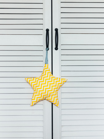 A close-up of a white-yellow soft star toy hangs on the handle of a white cabinet-screen. Light home interiorの写真素材