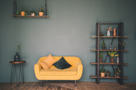 Interior design room or studio. Furniture against a green wall and wooden floor - a wooden table with a vase, a yellow sofa with cushions, a wardrobe with flowers and plants, a hanging shelfの写真素材