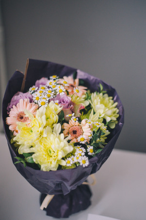 Close-up of a bouquet of colorful flowers in purple packaging stands on a white table on a blurred gray backgroundの写真素材