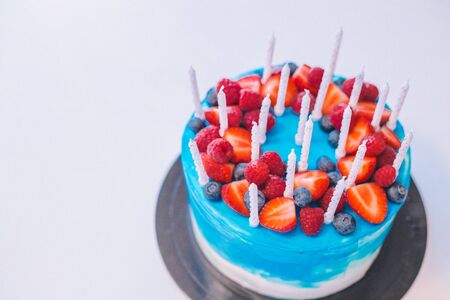 Close-up festive blue and white cake with candles and fruit decoration: strawberries, raspberries, blueberries. Cake for birthday, holiday and anniversary. Place for textの写真素材