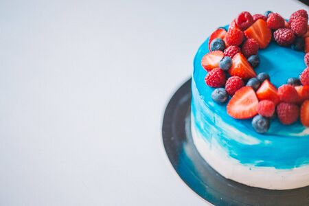 Close-up festive blue and white cake decorated with fruits: strawberries, raspberries, blueberries. Cake for birthday, holiday and anniversary. Space for textの写真素材