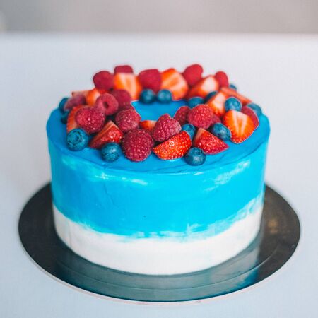 Close-up festive blue and white cake decorated with fruits: strawberries, raspberries, blueberries. Cake for birthday, holiday and anniversaryの写真素材