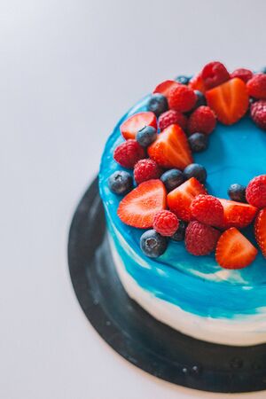 Close-up festive blue and white cake decorated with fruits: strawberries, raspberries, blueberries. Cake for birthday, holiday and anniversaryの写真素材