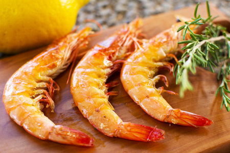 Grilled Shrimps Served on a Wooden Plate With Lemon and Rosemary. Three Grilled Seasoned Shrimps Closeup.の写真素材