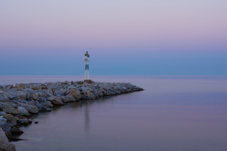 Lighthouse at Sunrise on the Rocky Coast. Dawning and Calm Sea in the Background.の写真素材