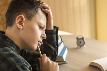 Young Boy Thinking Over a Book on Desk at Homeの写真素材