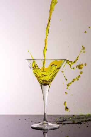 Yellow Cocktail Splashing From Martini Glass Isolated on White Background. Bar Commercials Concept.の写真素材