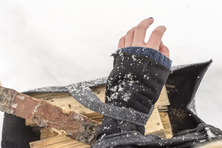Female Hand Covered with Snow Holding Basket Full of Firewoodの写真素材