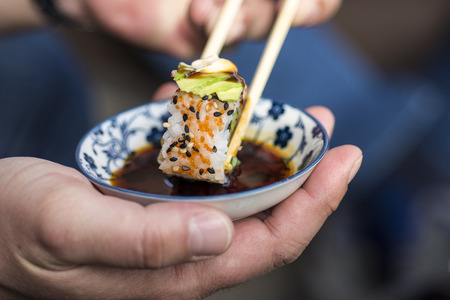 Male Hand Holding Chopsticks to Dip Sushi Roll in the Soy Sauceの写真素材