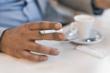 Cigarette in Male Hand With a Cup of Coffee. Smoking Addiction Concept.の写真素材