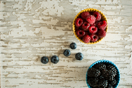 Raspberries and Blackberries in Ceramic Bowls on Rustic Backgroundの写真素材