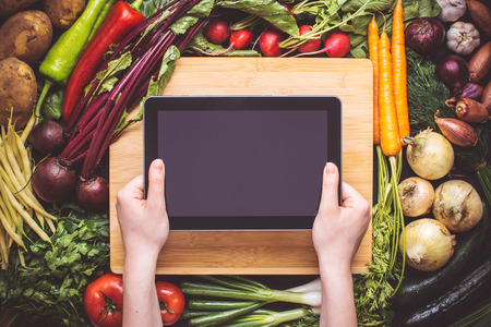 Hands with Tablet over Fresh Organic Vegetables Background. Vegetarian Food Recipes.の写真素材