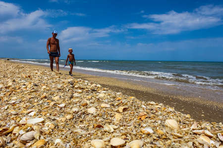 A man with a child on the shore of the Caspian Sea with shells. Dagestan. Russia 2021