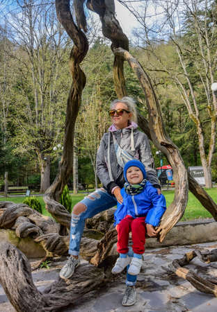 A girl with a child on the branches of a tree on the street in Borjomi, on a rainy day. Georgia 2019.の写真素材