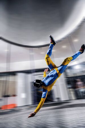Hobbies. Skydiver is flying in wind tunnel. Extreme people in blue and yellow suit make air jump. Air sport as a way of life. Skydiving team.の写真素材