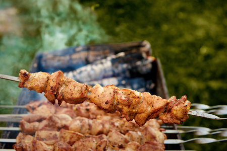 Pieces of delicious barbecued meat on skewer cooking on hot coals. Roast pork meat cooked on grill. Barbecue party on the nature. Close up top view.の写真素材
