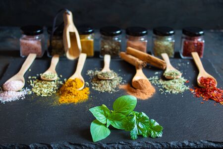 Spices and herbs of various colors in wooden spoons on black slate stoneの写真素材