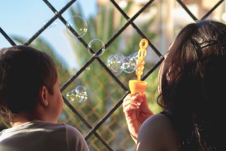 Mother and son blowing soap bubbles out the window during coronavirus quarantine