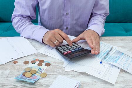 Young man calculates family accounts with the calculator during the crisis following the covid-19 pandemicの写真素材