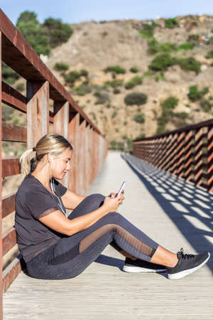 Young athlete woman sitting on the floor with mobile phone and headphonesの写真素材