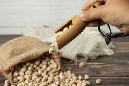 Hand pouring chickpeas into sack on wooden tableの写真素材