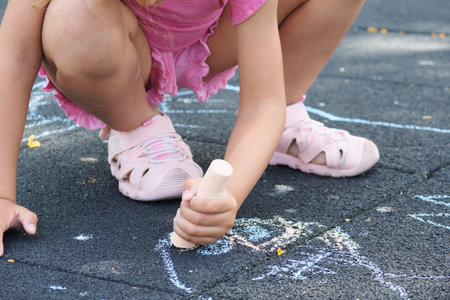 Unrecognizable little girl drawing on the floor of a playground with colored chalk.の写真素材