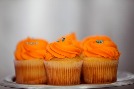 Creamy orange cupcakes with blue sprinkles on a platterの写真素材