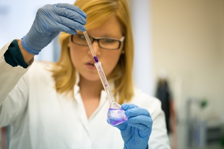 young female scientist in university laboratory works with colorful liquids