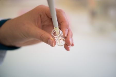 two hands of young female scientist working with pipette and laboratory flaskの写真素材
